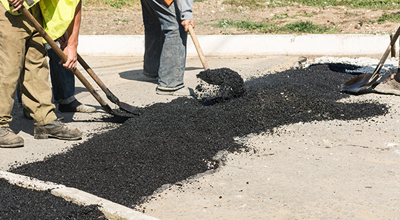 workers applying asphalt to a surface with shovels for road construction repair 2 layers of asphalt