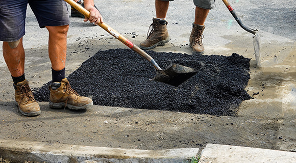 workers repairing asphalt surface with shovels in construction site