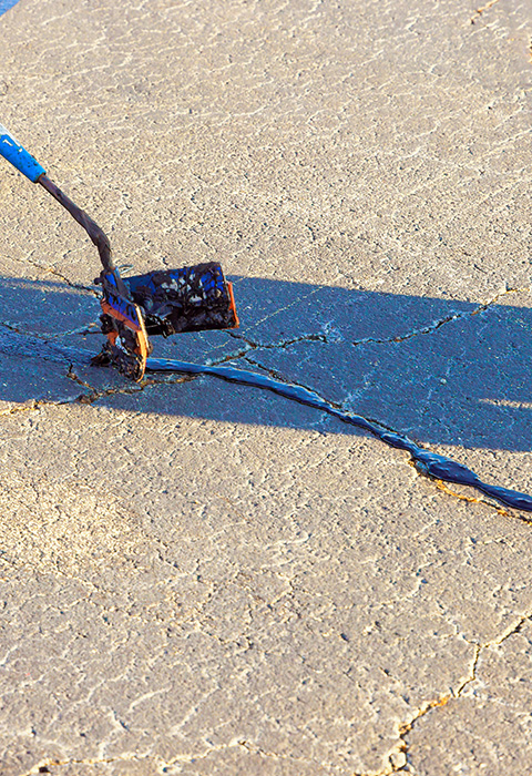 a person using a tool to seal cracks in pavement with a black material ideal for repair and maintenance purposes