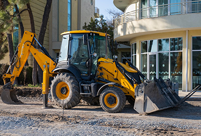 yellow backhoe loader parked near modern building construction site with gravel showing 5 essential tools for excavation