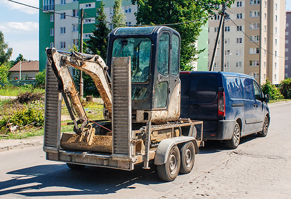 excavator on a trailer behind a van on a residential street with buildings in the background construction equipment 6 tools 6 activities 6 sites 6 machines